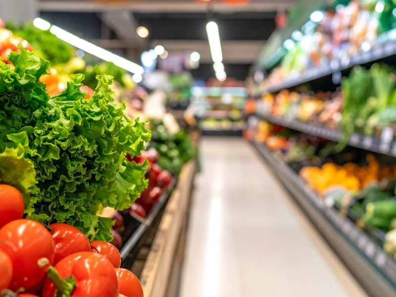 Pasillo de supermercado con tomates y lechuga fresca en la sección de frutas y verduras.