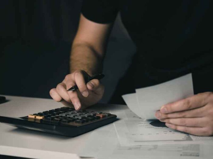 Manos usando una calculadora y revisando documentos financieros para calcular costos y gastos del negocio.