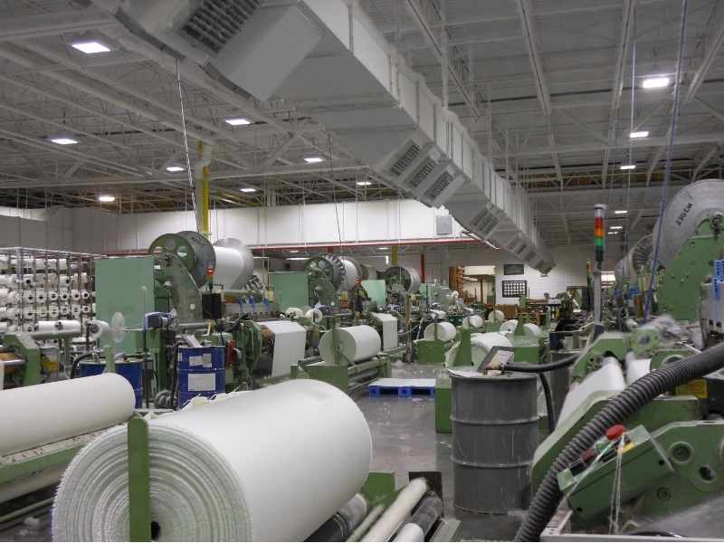 manufactura, Interior de una planta textil con maquinaria industrial y rollos de material en producción.
