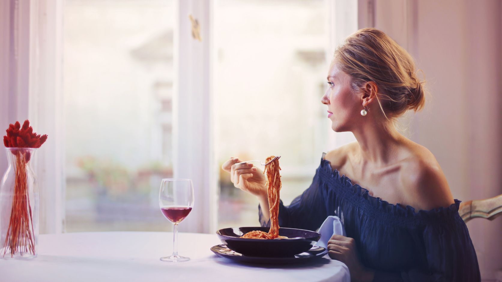Mujer sentada en un restaurante disfrutando de un platillo acompañado de una copa de vino tinto.