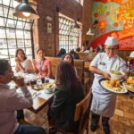 Interior de un pequeño restaurante tradicional latinoamericano con mesas de madera y personal atendiendo a los clientes.