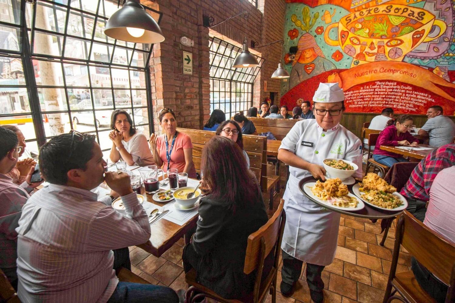 Interior de un pequeño restaurante tradicional latinoamericano con mesas de madera y personal atendiendo a los clientes.